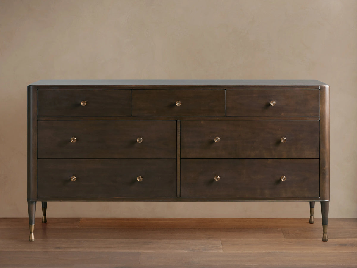 Laurent Seven-Drawer Dresser in dark wood, featuring seven drawers with patinaed brass knobs, stands on slender brass-accented legs.