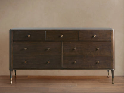 Laurent Seven-Drawer Dresser in dark wood, featuring seven drawers with patinaed brass knobs, stands on slender brass-accented legs.