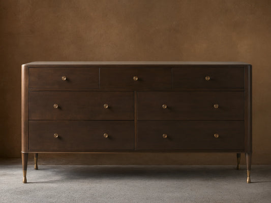 Laurent Seven-Drawer Dresser in dark wood, featuring seven drawers with patinaed brass knobs, stands on slender brass-accented legs.