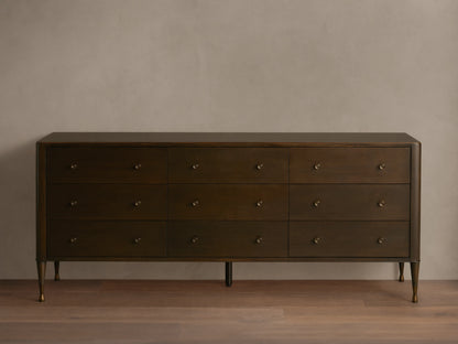 Long, dark brown Laurent Nine-Drawer Dresser with three rows of drawers, brass knobs, and tapered brass feet on a wooden floor.