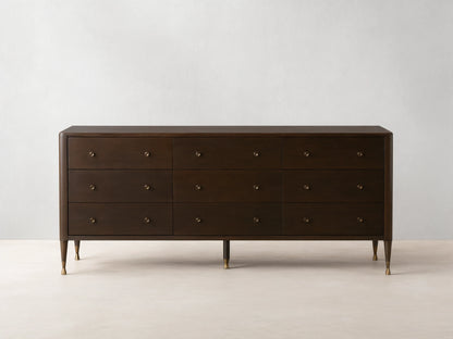 Long, dark brown Laurent Nine-Drawer Dresser with three rows of drawers, brass knobs, and tapered brass feet on a wooden floor.