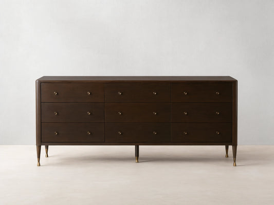 Long, dark brown Laurent Nine-Drawer Dresser with three rows of drawers, brass knobs, and tapered brass feet on a wooden floor.