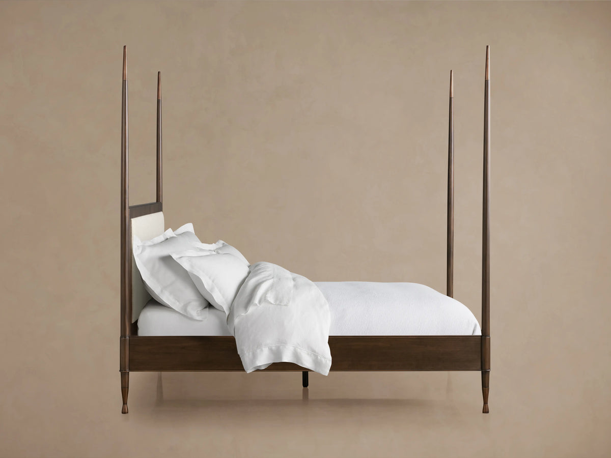 Laurent Bed with tall, slender posts at each corner, dark mahogany finish, white bedding, and patinaed brass finials.