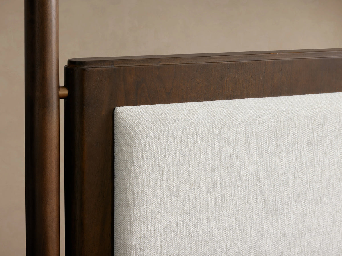 Laurent Bed's headboard featuring solid mahogany wood with cherry veneer and beige upholstered fabric. Patinaed brass finial is visible.