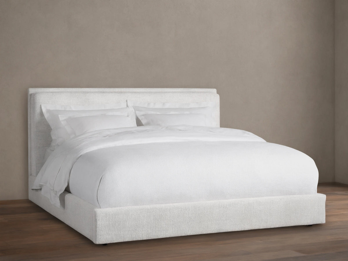 Light cream textured fabric upholstered Lennon Bed with matching headboard and frame, dressed with white bedding, on a wood floor.