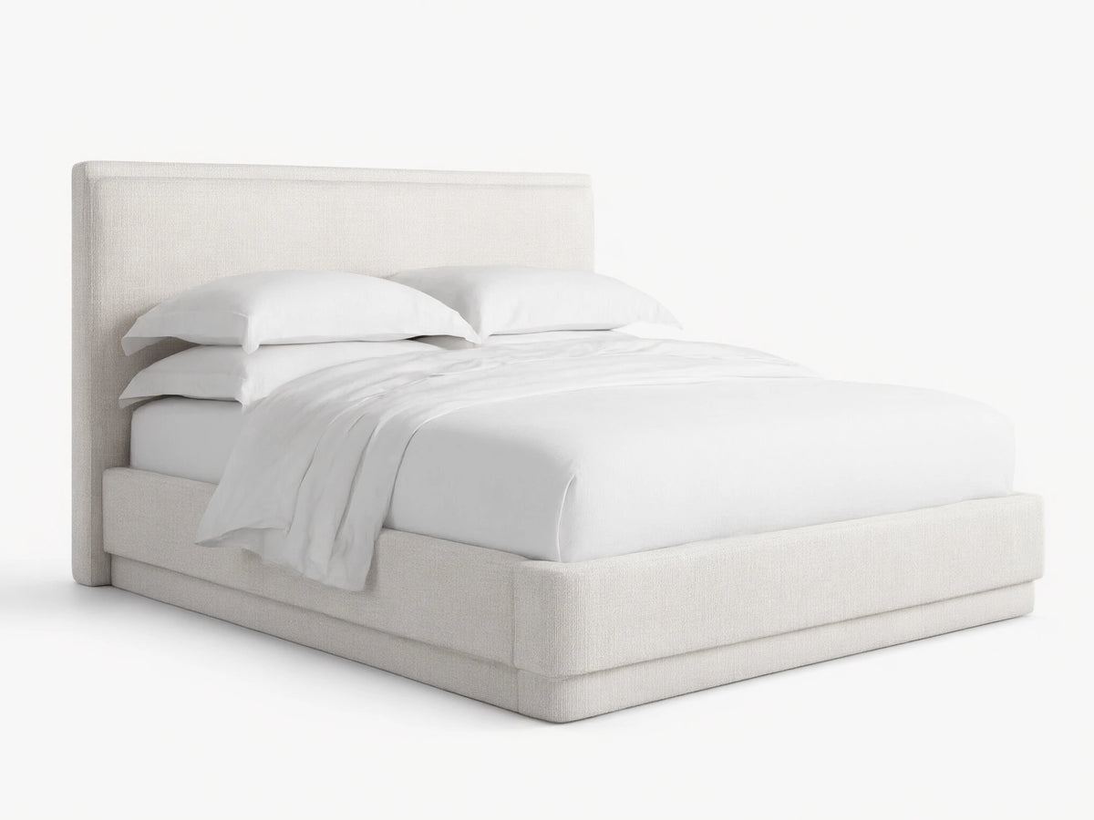 Light cream textured fabric upholstered Lennon Bed with matching headboard and frame, dressed with white bedding, on a wood floor.