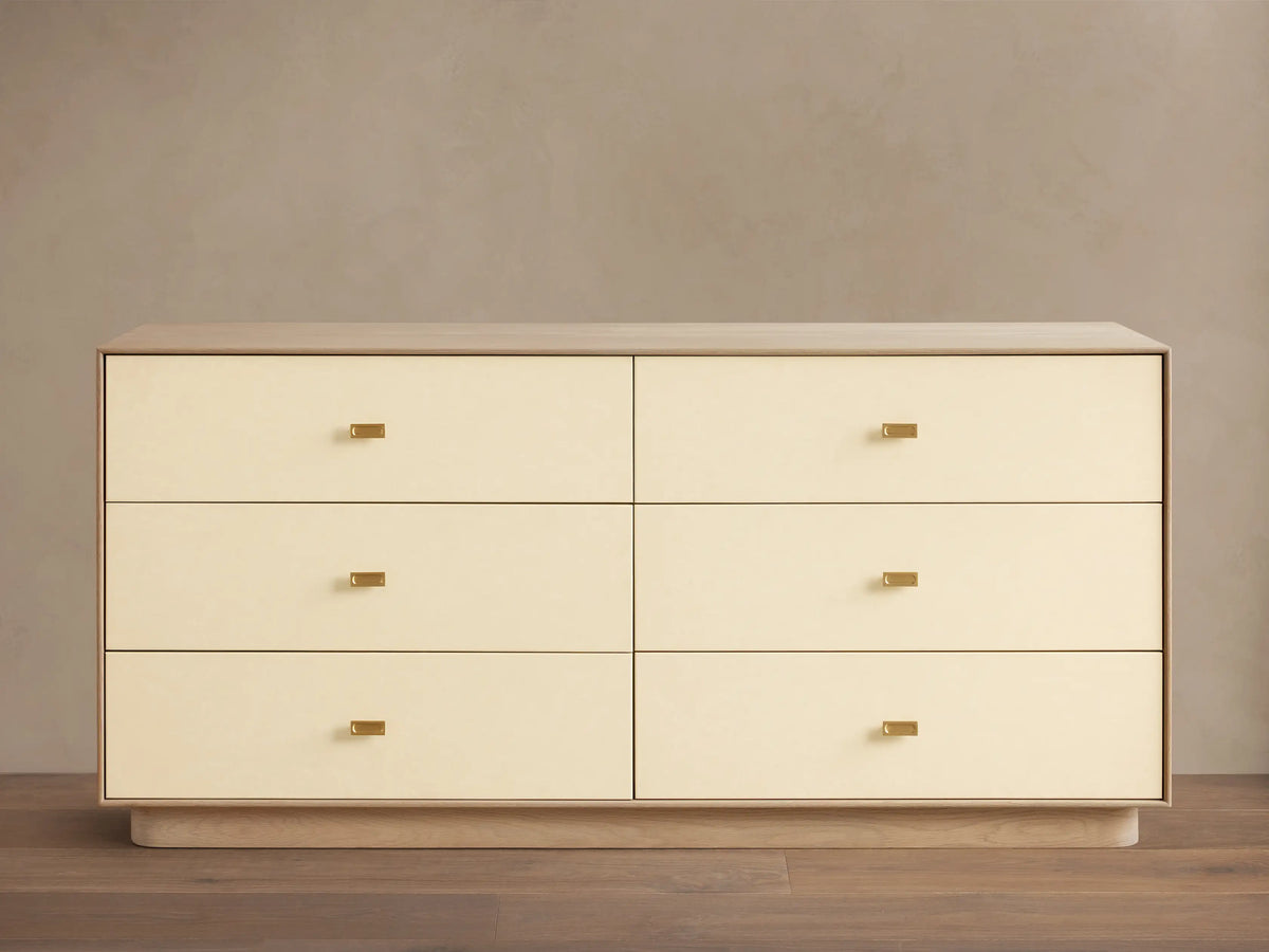 Front view of the cream Lowen Six-Drawer Dresser with light oak wood veneer frame, faux leather drawer fronts, and champagne brass pulls.