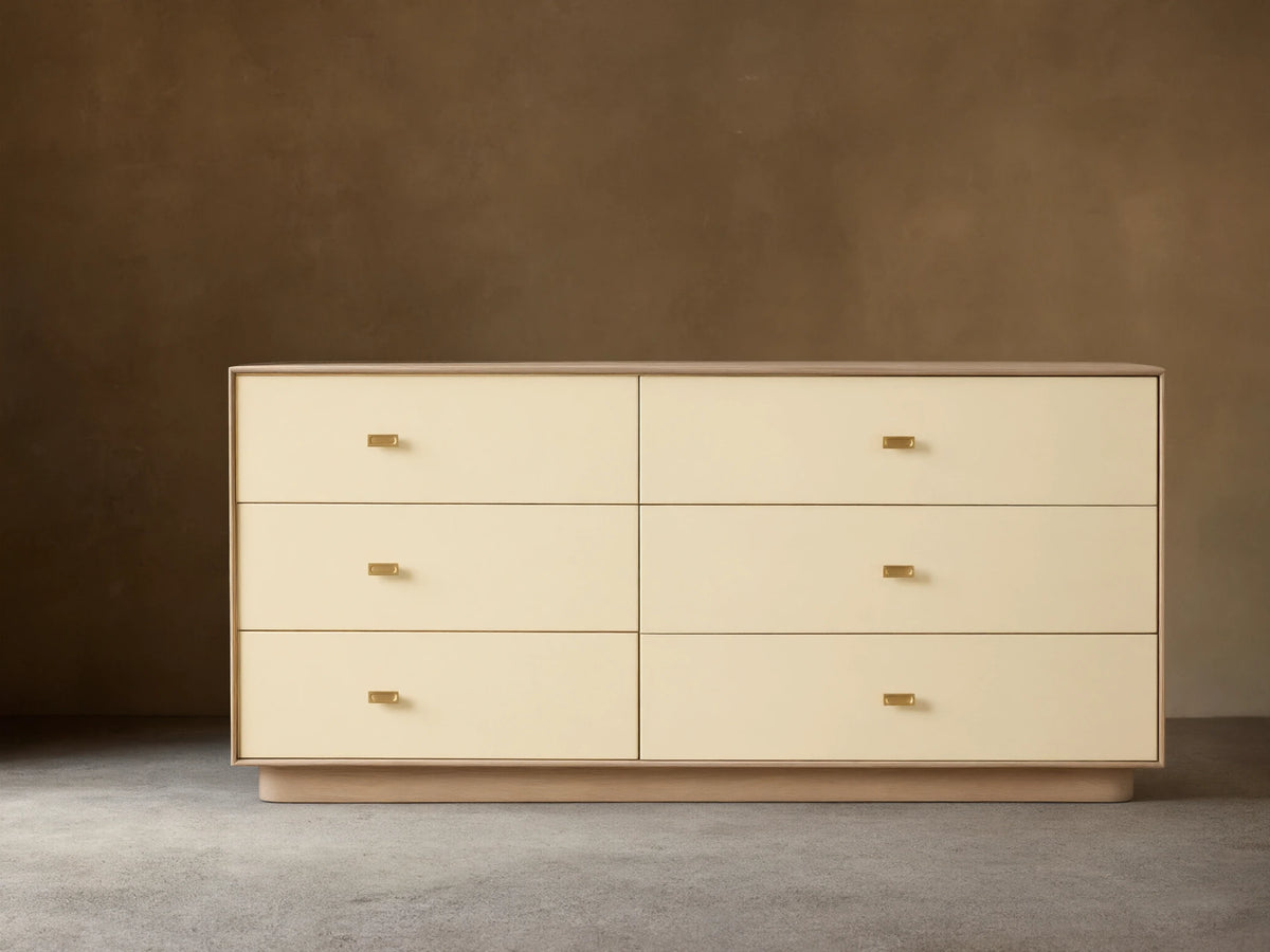 Front view of the cream Lowen Six-Drawer Dresser with light oak wood veneer frame, faux leather drawer fronts, and champagne brass pulls.