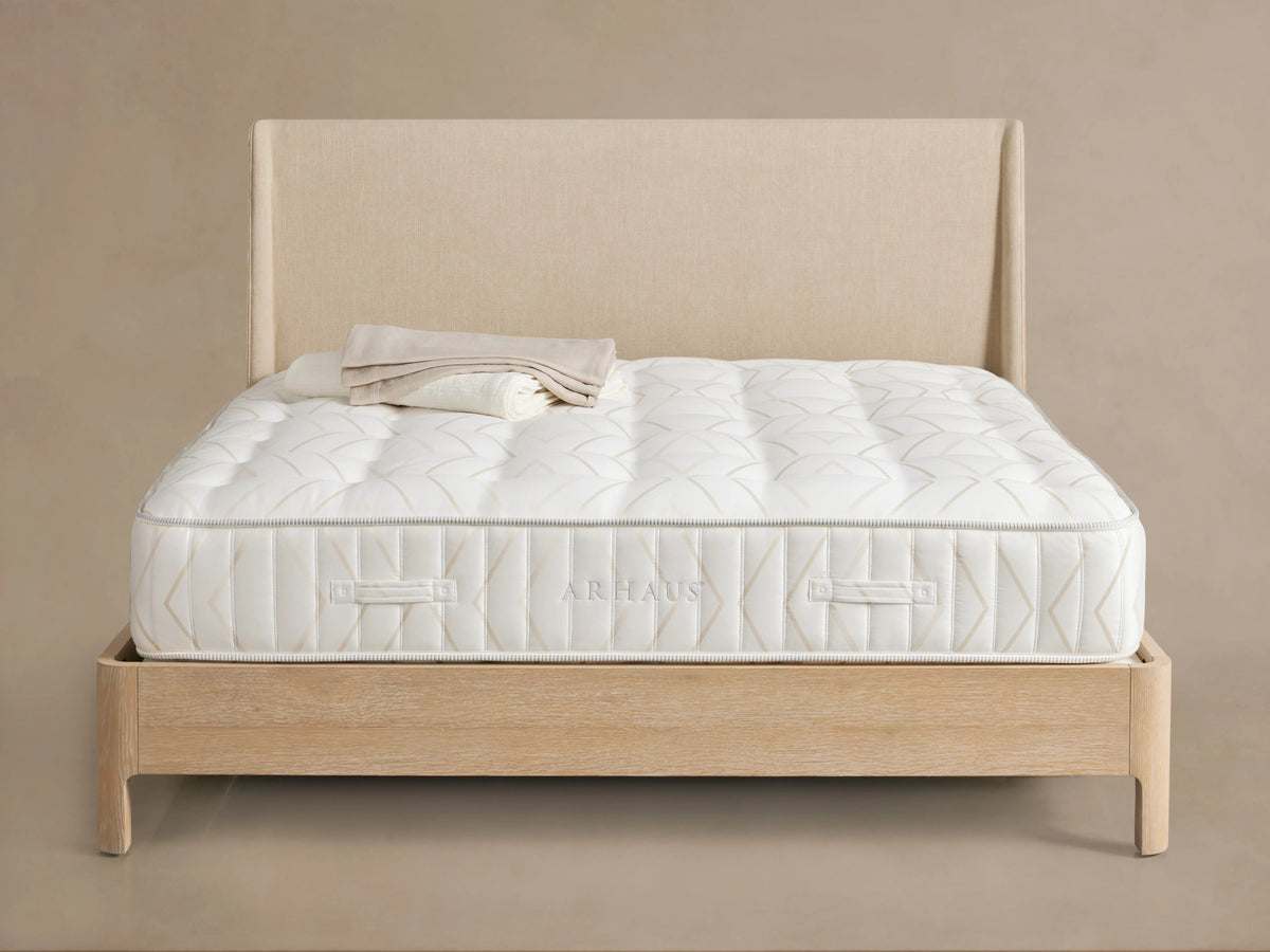 Luxury Firm Mattress on a wooden bed frame with a beige fabric headboard, featuring a quilted white surface and rectangular patterns.