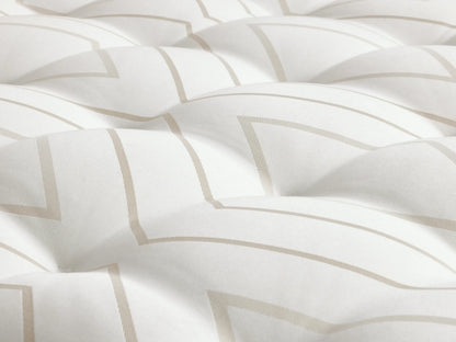 A luxury firm mattress on a light wood bed frame with a beige upholstered headboard. The white mattress features hand-tufting and two folded sheets on top.