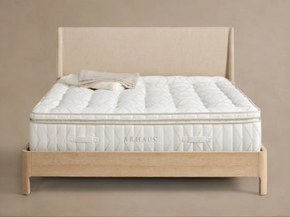 Luxury Plush Mattress on a wooden bed frame in a minimalist room. The mattress has a white, quilted surface with visible hand-tufting details.