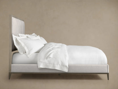 Malone Upholstered Bed in side view, featuring a light neutral fabric with matched panels and channel stitching, paired with white bedding.