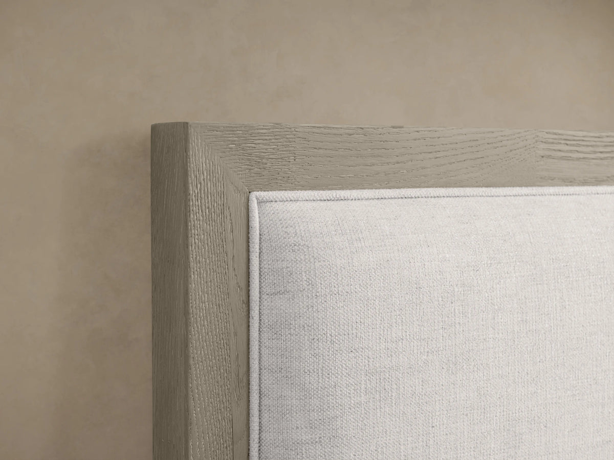 Malone Upholstered Bed with light neutral fabric headboard, wooden frame in grayish tone, close-up on corner detail.