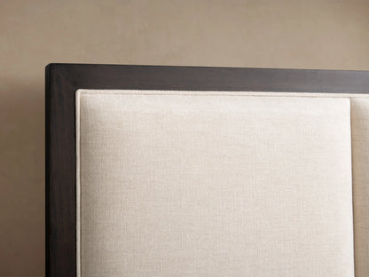 Close-up of Malone Upholstered Bed headboard. Dark wood frame encases light cream, channel-stitched fabric panel with weave texture.