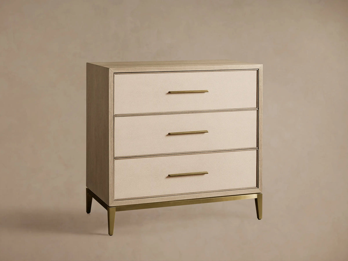 Malone Three-Drawer Chest. Light wood frame, textured bone drawer fronts with gold pulls. Top closed, middle and bottom partially open.