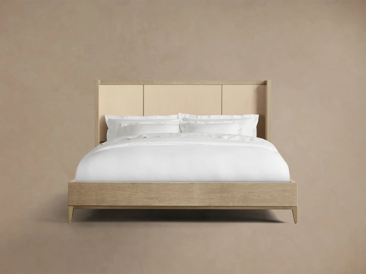 Front 3/4 view of a Bone Malone Shelter Bed with an oak frame, segmented light reconstituted leather headboard inserts, and metallic leg accents.
