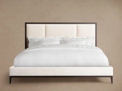Upholstered bed with a neutral-colored headboard featuring three stitched panels, black wooden frame, and white bedding on wooden floor.