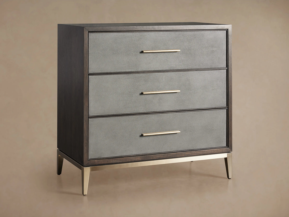 Malone Three-Drawer Chest with dark wood frame, gray textured fronts, metallic handles, and sleek metallic legs on wooden floor.