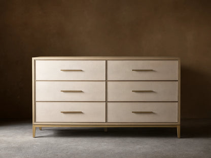 Front view of the Bone Malone Six-Drawer Dresser, featuring light beige textured shagreen drawer fronts, gold bar pulls, and tapered gold legs.