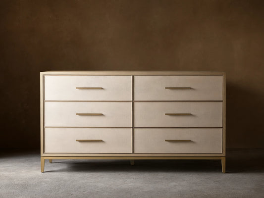 Front view of the Bone Malone Six-Drawer Dresser, featuring light beige textured shagreen drawer fronts, gold bar pulls, and tapered gold legs.
