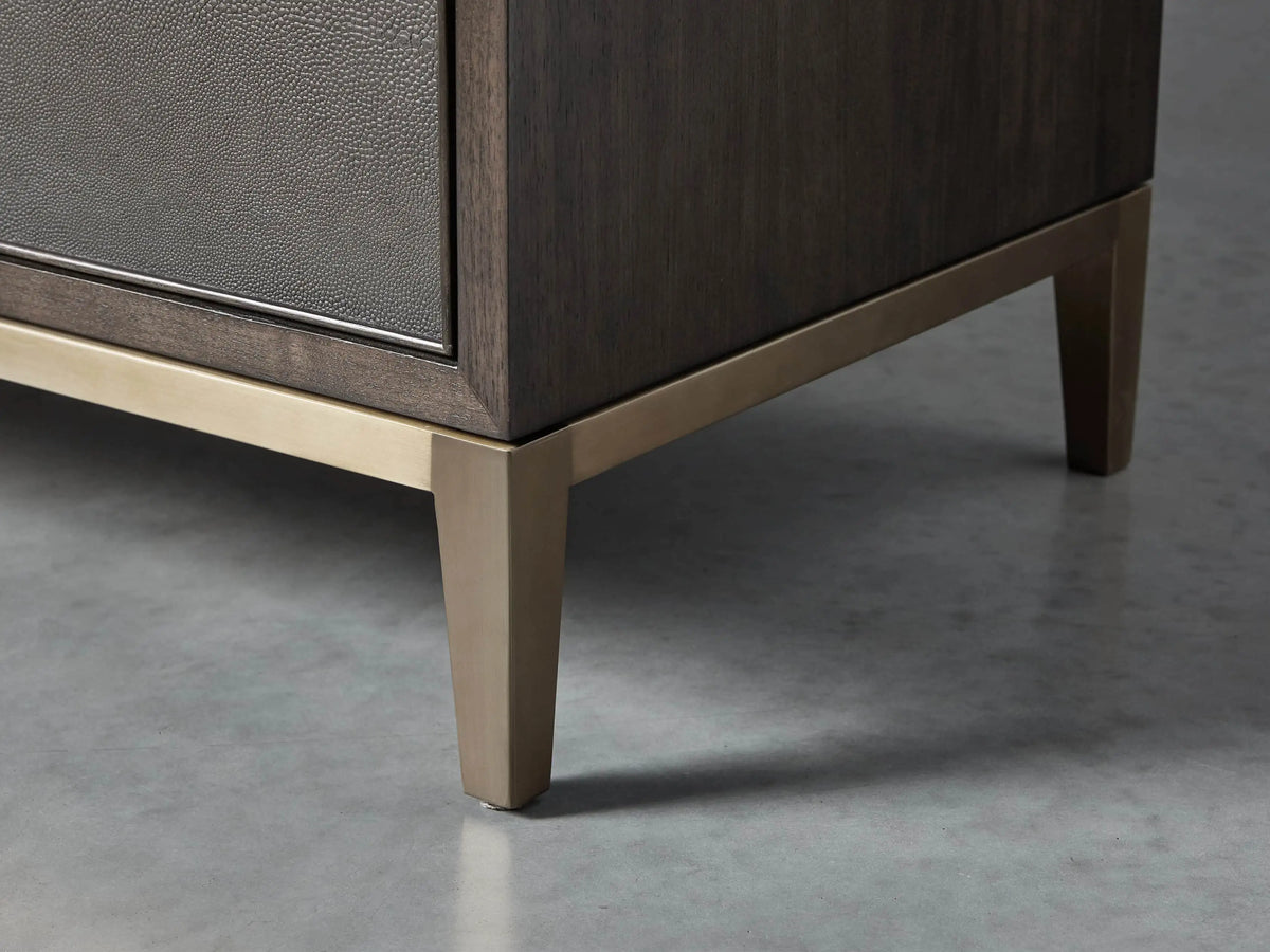 Close-up of the bottom right of the dark wood Malone Six-Drawer Dresser, with a textured dark gray shagreen leather drawer front and a warm metallic base.