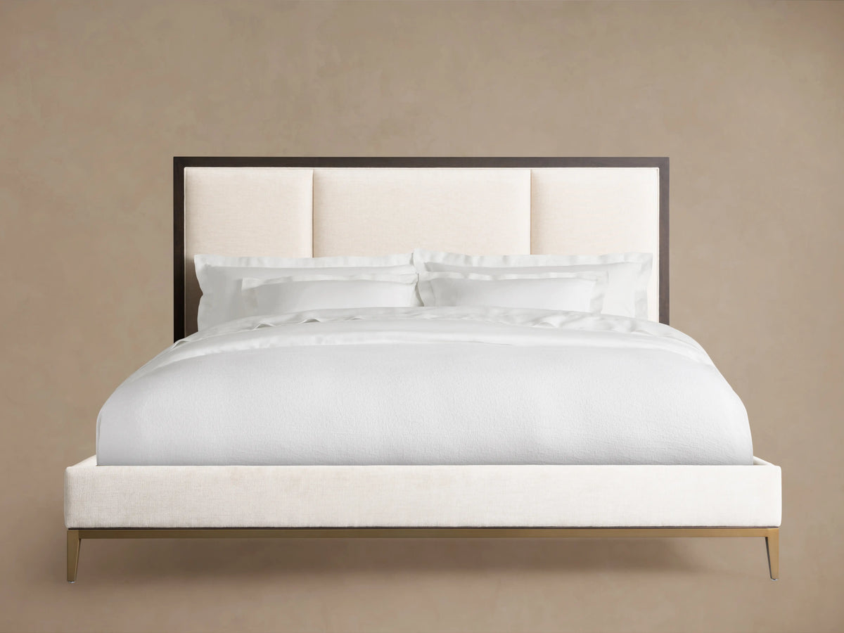 Malone Upholstered Bed with a neutral-toned headboard featuring three channel-stitched panels. Frame in dark wood, set in a spacious room.