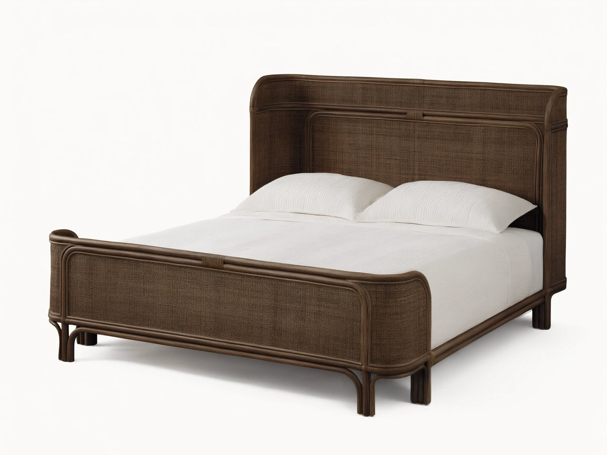 Maya Bed: Dark brown woven rattan bed frame with curved headboard & footboard, dressed with white sheets & pillows on a wood floor.