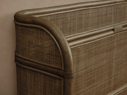 Maya Bed: dark brown woven rattan mesh bed frame with curved headboard and footboard, dressed with white bedding, against a light wall.