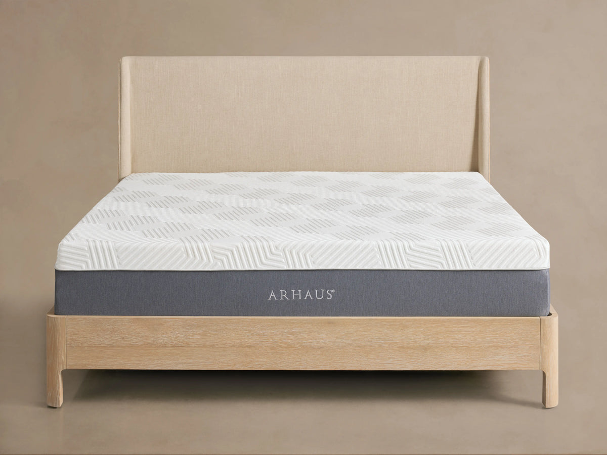 Memory Foam Firm Mattress on a light wood bed frame with a beige upholstered headboard, showing a textured white cover.