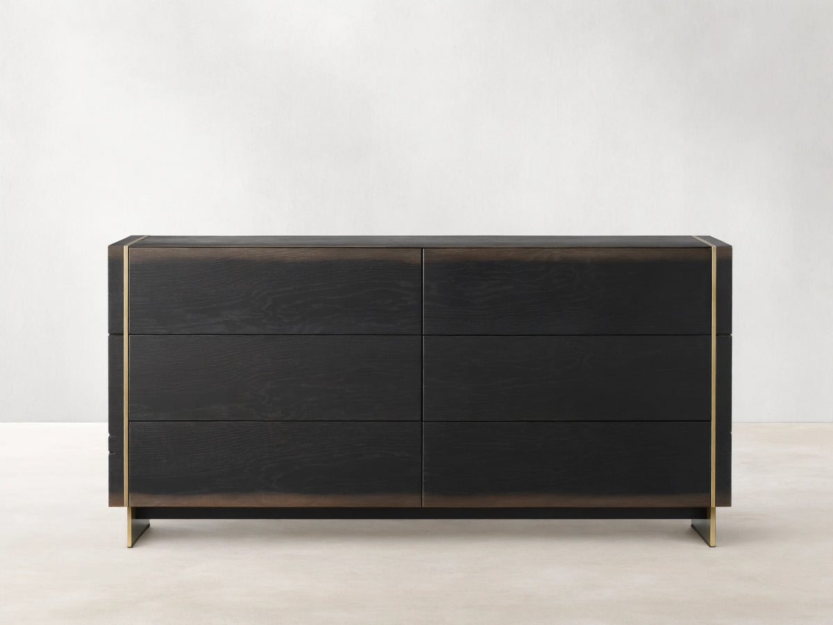 Mihaela Six-Drawer Dresser in dark oak with six drawers, featuring metallic brass accents on the edges, against a beige wall.