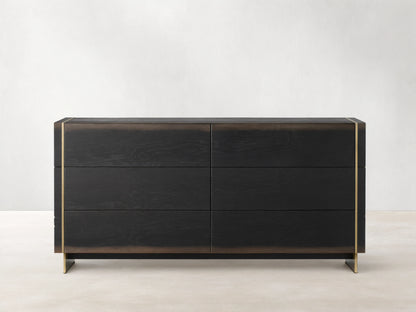 Mihaela Six-Drawer Dresser in dark oak with six drawers, featuring metallic brass accents on the edges, against a beige wall.