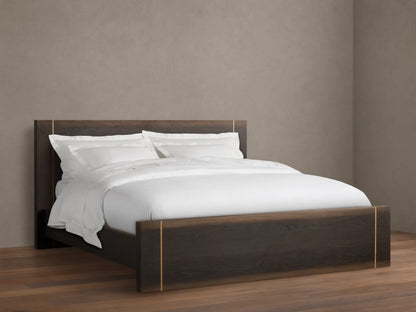 Mihaela Bed with dark oak frame, metallic brass accents, white bedding, on a wooden floor, set against a beige wall.