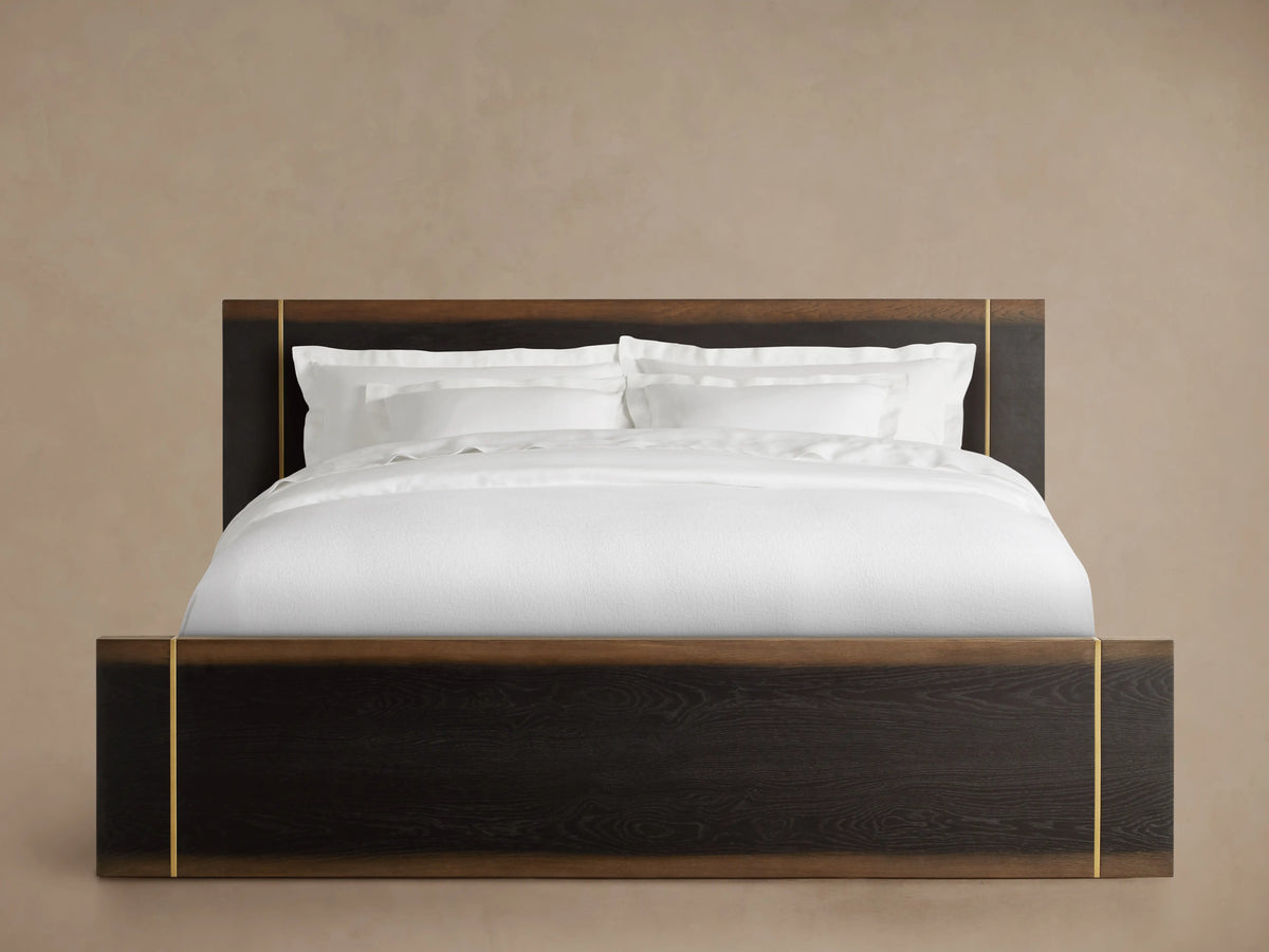 Mihaela Bed side view displaying a dark wood frame with hand-carved detailing, white bedding neatly arranged and tucked in.