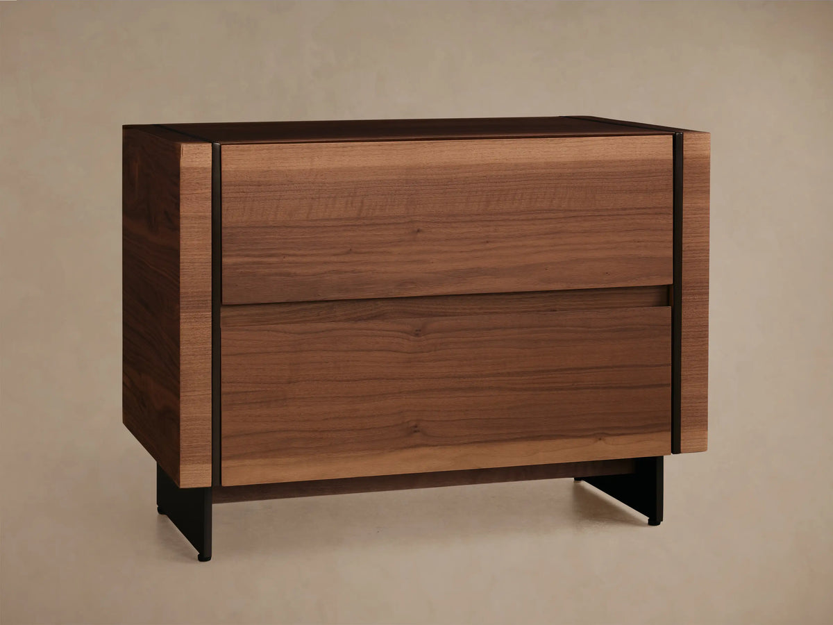 Mihaela Nightstand: A sleek walnut veneer nightstand with two hardware-free drawers, on dark metal legs, against a soft-toned wall.