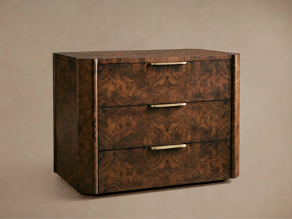 A wooden chest of drawers with three compartments, featuring a dark burl wood finish and sleek metallic handles, placed against a beige wall.