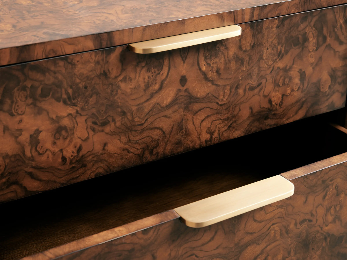 A three-drawer wooden chest with a rich, dark brown marbled texture and sleek, horizontal metallic handles, set against a soft beige background.