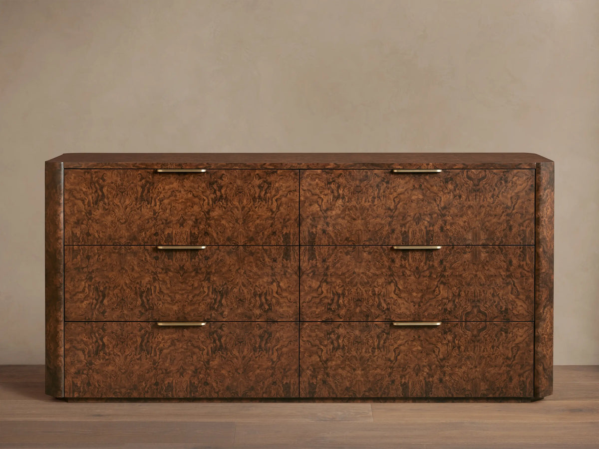 Wooden dresser with a textured, dark brown finish featuring six drawers. Each drawer has a sleek gold-toned handle. Set against a plain wall.