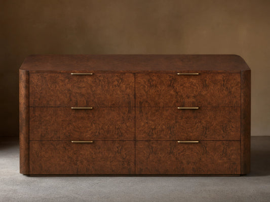 Wooden dresser with a textured, dark brown finish featuring six drawers. Each drawer has a sleek gold-toned handle. Set against a plain wall.