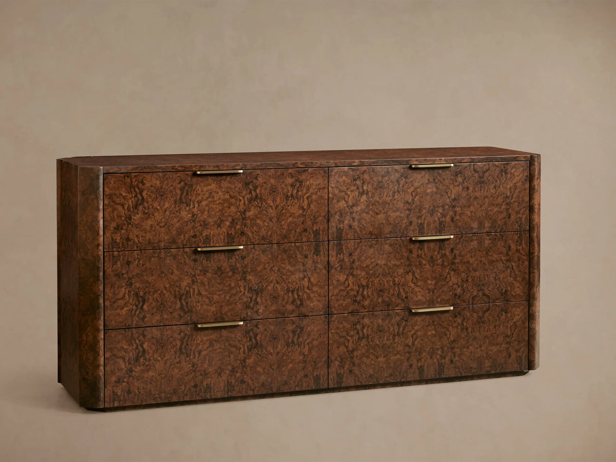 Wooden dresser with a textured, dark brown finish featuring six drawers. Each drawer has a sleek gold-toned handle. Set against a plain wall.