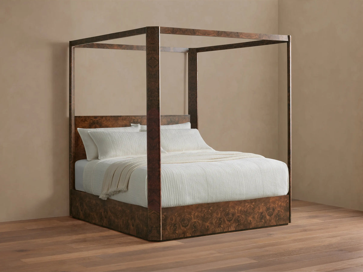 Wooden four-poster bed with white bedding and pillows, set in a minimalistic room with beige walls and hardwood flooring.