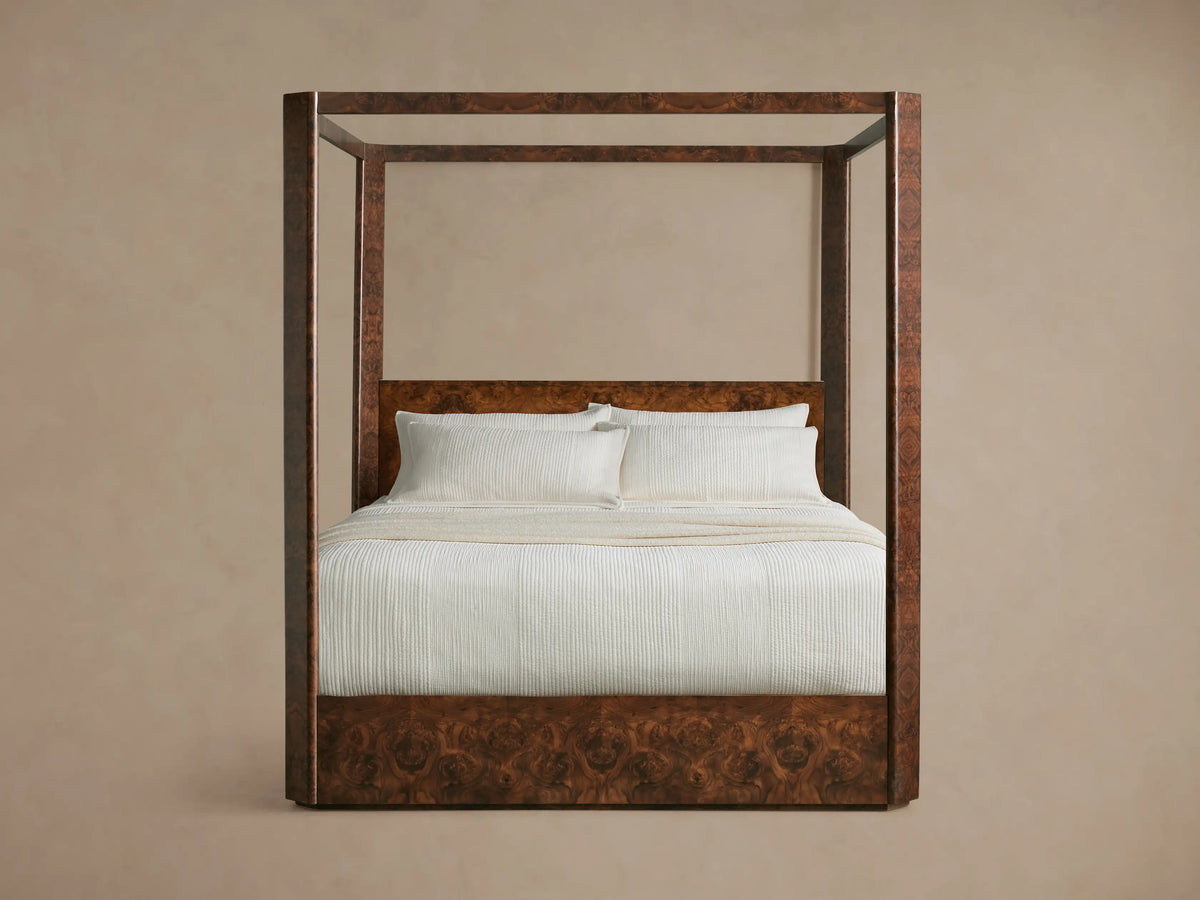 Wooden four-poster bed with white bedding and pillows, set in a minimalistic room with beige walls and hardwood flooring.