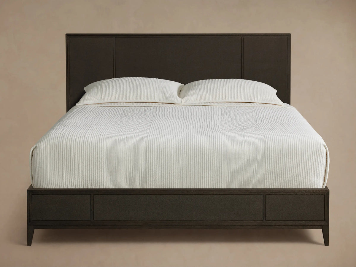 Front view of the dark brown Olina Bed, featuring a textured raffia headboard and footboard, with white bedding.