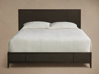 Front view of the dark brown Olina Bed, featuring a textured raffia headboard and footboard, with white bedding.