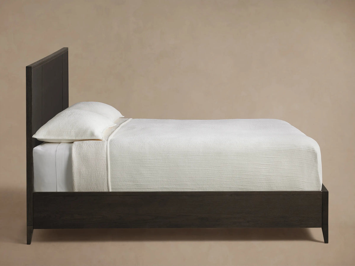 Close-up of the angled dark oak wood frame and dark grey textural raffia panel of the Olina Bed.