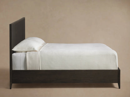 Close-up of the angled dark oak wood frame and dark grey textural raffia panel of the Olina Bed.