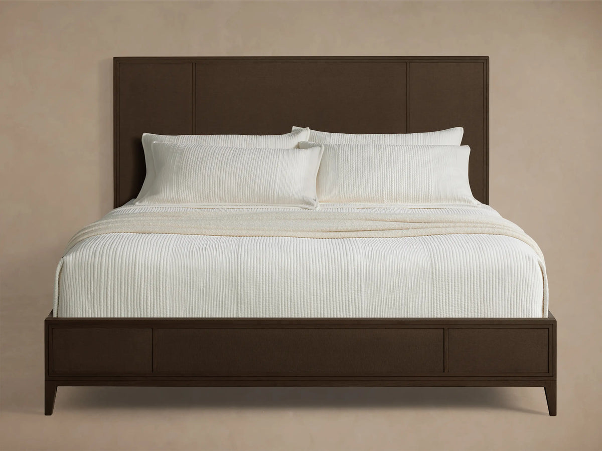 Front view of the dark brown Olina Bed, featuring textural raffia panels on the headboard and footboard, dressed with white bedding.