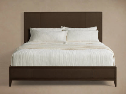 Front view of the dark brown Olina Bed, featuring textural raffia panels on the headboard and footboard, dressed with white bedding.