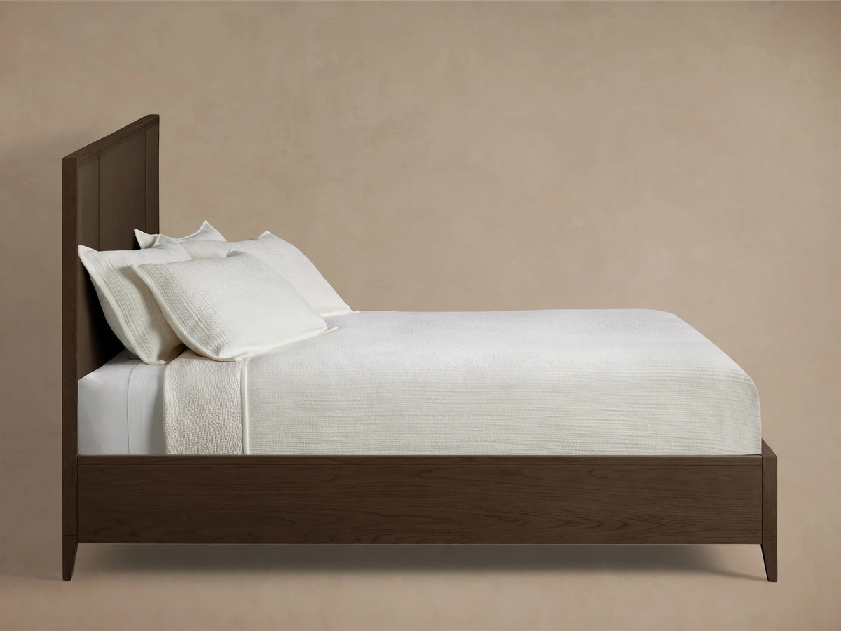 Close-up of the dark brown oak wood frame and textural raffia panel of the Olina Bed headboard.