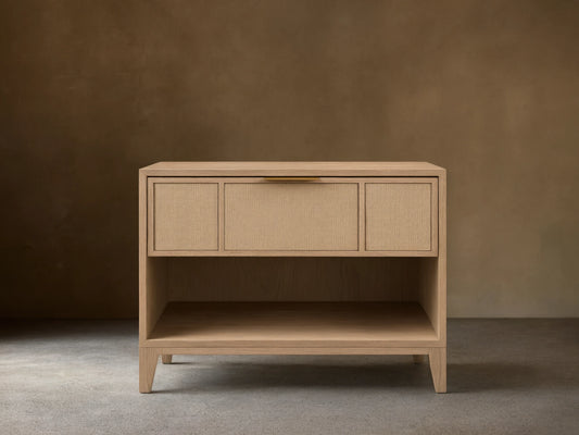 Front view of the light oak Olina Open Nightstand with a raffia drawer front, brass pull, and an open storage shelf.