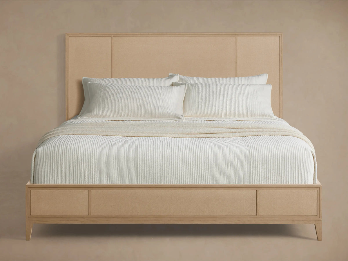 Front view of the Olina Bed, a light oak wood frame with light beige textural raffia headboard and footboard, styled with white bedding.